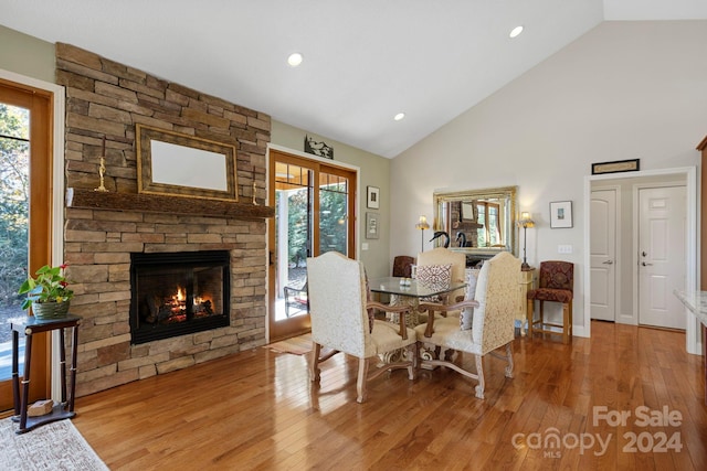 dining room with a stone fireplace, high vaulted ceiling, and light wood-type flooring