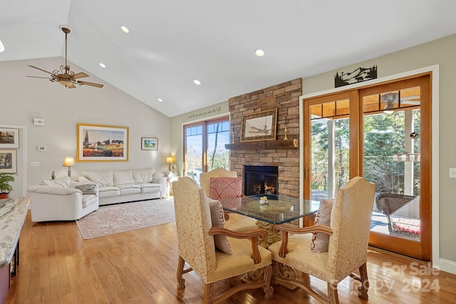 dining space with light hardwood / wood-style floors, a stone fireplace, a healthy amount of sunlight, and ceiling fan