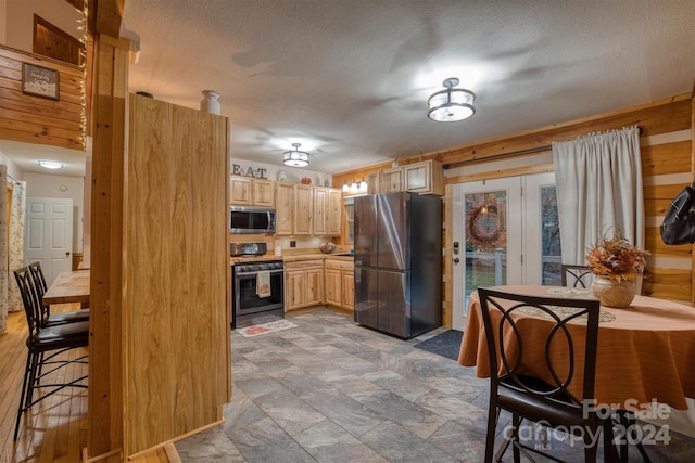 kitchen featuring wooden walls, stainless steel appliances, a textured ceiling, and light brown cabinets