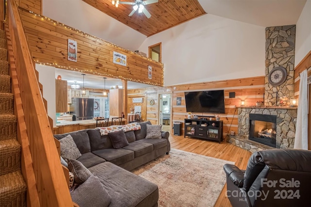 living room featuring hardwood / wood-style flooring, wood ceiling, a stone fireplace, ceiling fan, and high vaulted ceiling