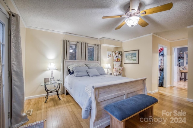 bedroom featuring ceiling fan, a textured ceiling, ornamental molding, light hardwood / wood-style floors, and a closet