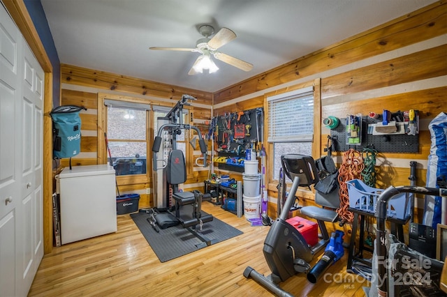 exercise area featuring light wood-type flooring, wooden walls, and ceiling fan