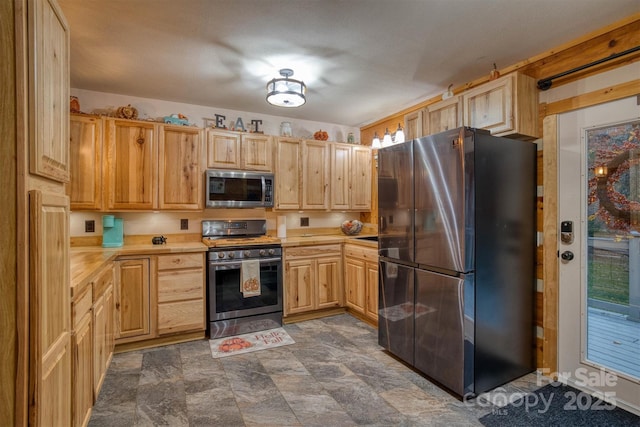 kitchen featuring light countertops, stone finish floor, appliances with stainless steel finishes, and light brown cabinets