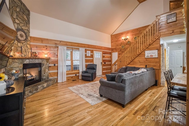 living area featuring stairway, high vaulted ceiling, wooden walls, a fireplace, and wood-type flooring