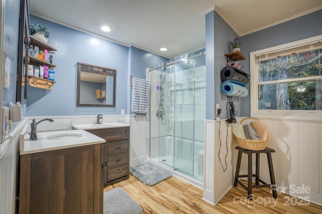 bathroom featuring a wainscoted wall, two vanities, a sink, a shower stall, and crown molding