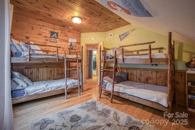 bedroom with lofted ceiling, wood walls, wood finished floors, and wainscoting