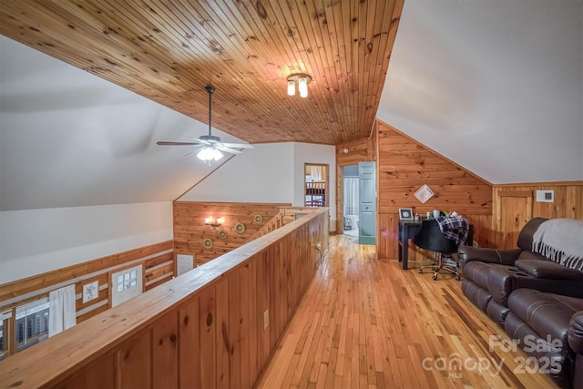 hallway with vaulted ceiling, an upstairs landing, wooden walls, and light wood-type flooring