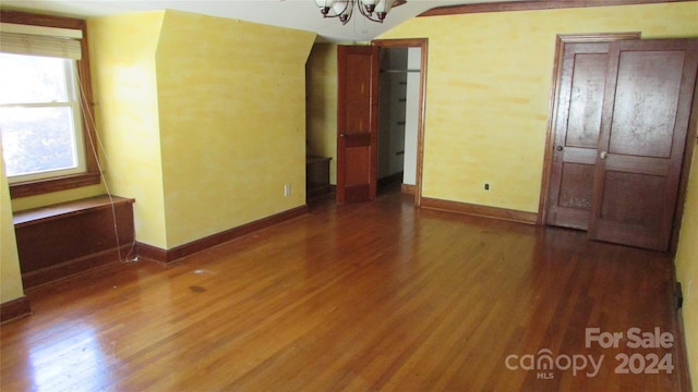 empty room with hardwood / wood-style floors, vaulted ceiling, and a chandelier