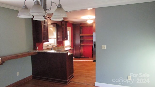 kitchen with kitchen peninsula, wood-type flooring, sink, crown molding, and decorative light fixtures