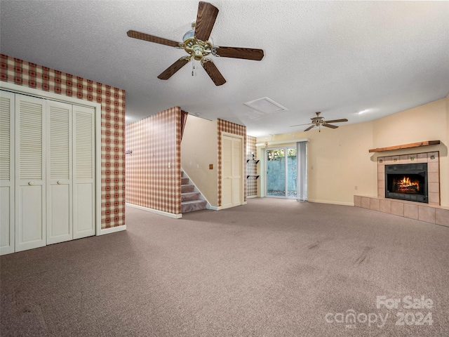 unfurnished living room with a tiled fireplace, carpet flooring, a textured ceiling, and ceiling fan