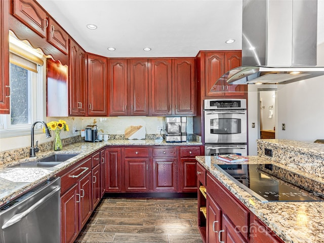 kitchen with appliances with stainless steel finishes, sink, island range hood, light stone counters, and dark hardwood / wood-style floors