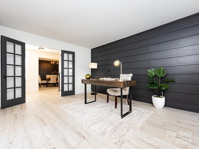 home office featuring french doors, light hardwood / wood-style floors, and wooden walls