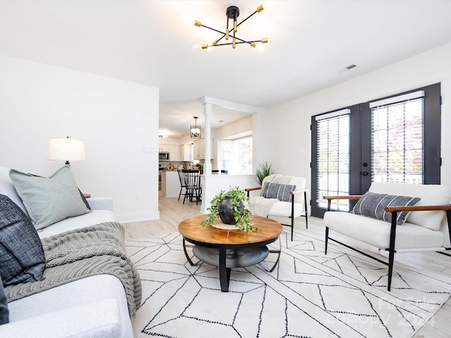 living room with light hardwood / wood-style floors, a notable chandelier, french doors, and plenty of natural light