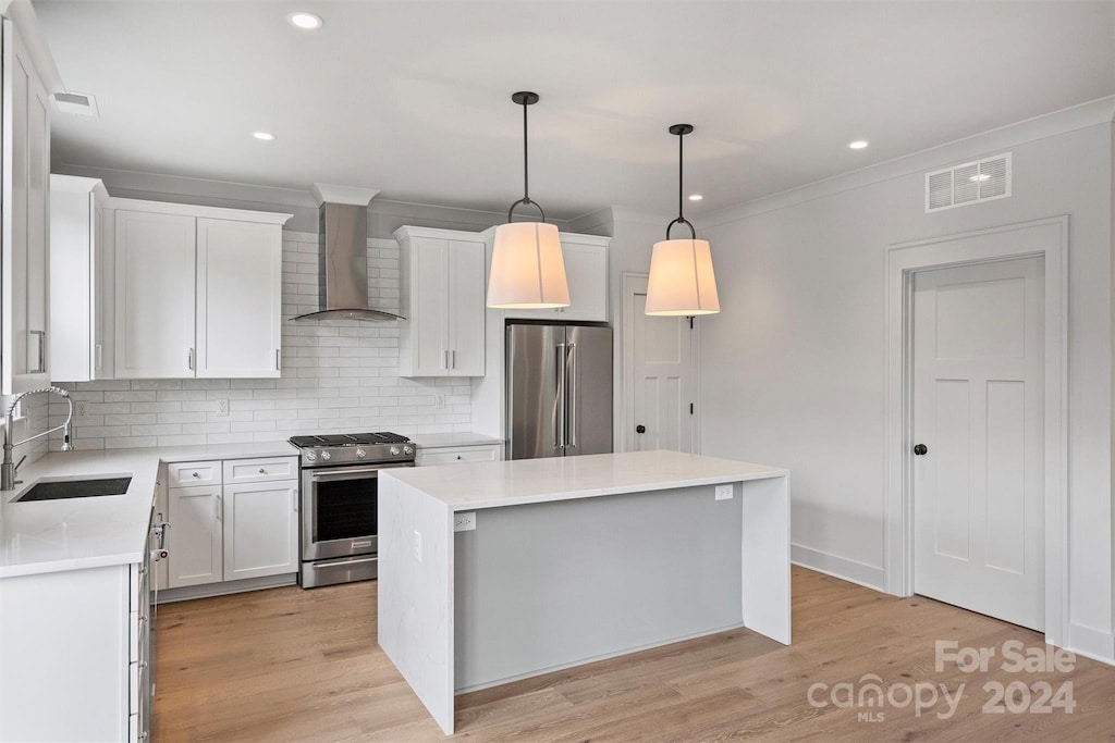 kitchen featuring a center island, sink, stainless steel appliances, wall chimney range hood, and white cabinets