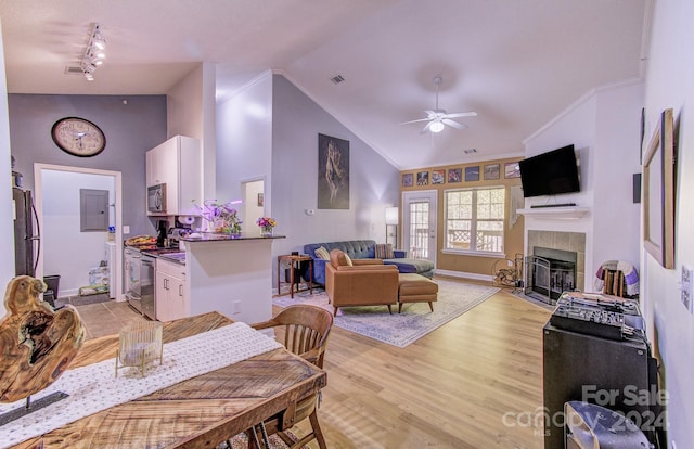 dining space with a tiled fireplace, light hardwood / wood-style flooring, ornamental molding, high vaulted ceiling, and ceiling fan