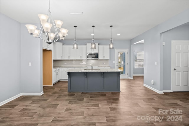 kitchen with pendant lighting, light stone countertops, an island with sink, and white cabinets