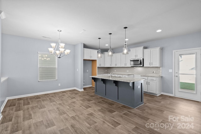 kitchen featuring light stone countertops, light wood-type flooring, white cabinetry, a breakfast bar area, and a kitchen island with sink