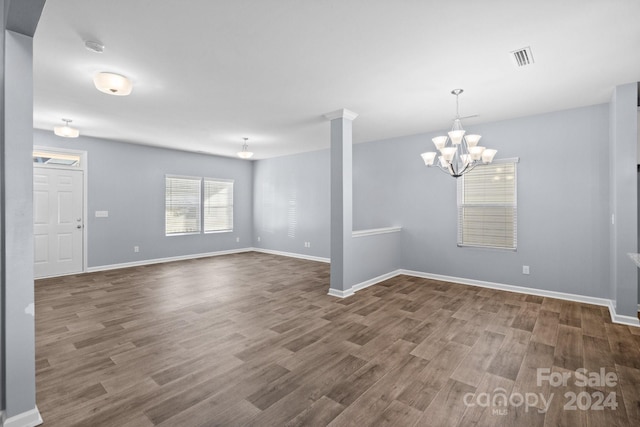 empty room with decorative columns, a chandelier, and dark hardwood / wood-style floors