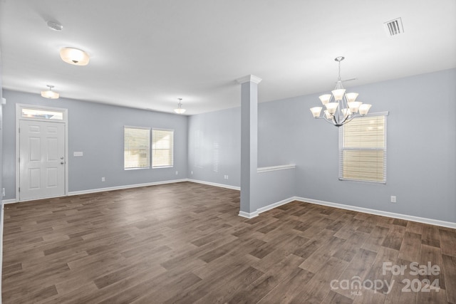 spare room featuring a chandelier, ornate columns, and dark hardwood / wood-style floors