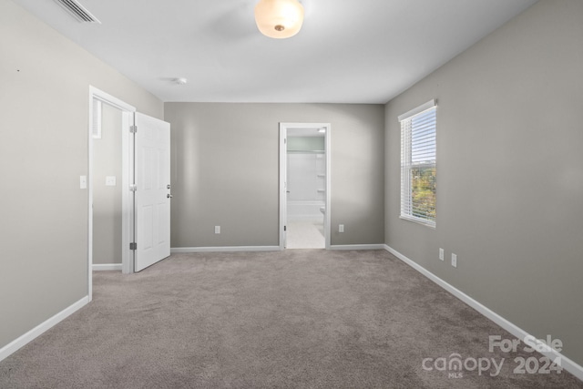 unfurnished bedroom with light carpet, a walk in closet, and ensuite bath