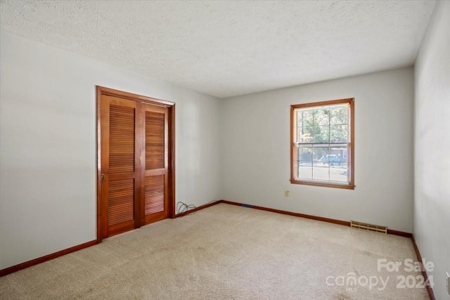 unfurnished bedroom featuring light carpet, a textured ceiling, and a closet