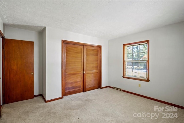 unfurnished bedroom featuring a closet, light carpet, and a textured ceiling