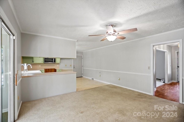 kitchen featuring sink, a textured ceiling, green cabinets, ornamental molding, and light colored carpet