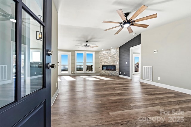 unfurnished living room featuring ceiling fan, dark hardwood / wood-style floors, a stone fireplace, and vaulted ceiling