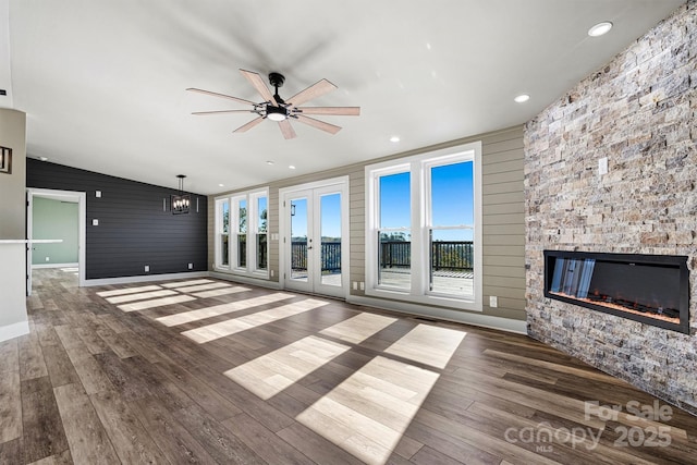 unfurnished living room featuring ceiling fan with notable chandelier, dark hardwood / wood-style flooring, lofted ceiling, and a fireplace