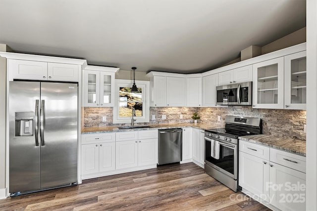 kitchen with pendant lighting, sink, light stone countertops, appliances with stainless steel finishes, and white cabinetry