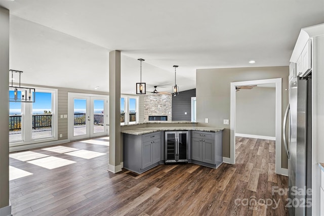 kitchen featuring stainless steel refrigerator, beverage cooler, light stone counters, lofted ceiling, and gray cabinets