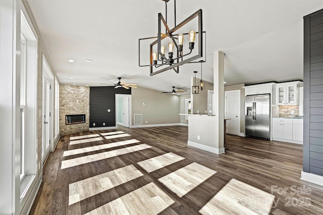 unfurnished living room featuring ceiling fan with notable chandelier, lofted ceiling, a fireplace, and dark wood-type flooring