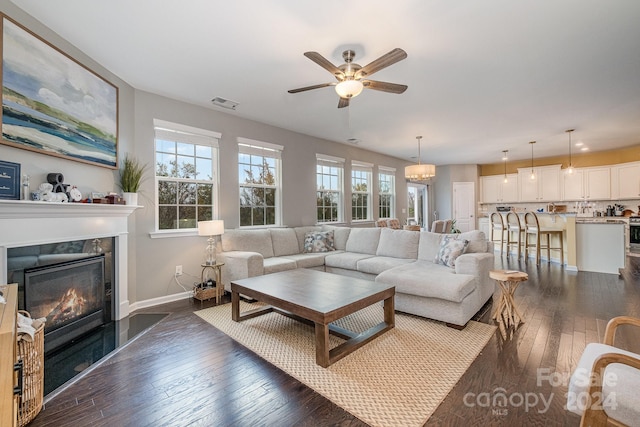 living room with dark wood-type flooring, a premium fireplace, and ceiling fan