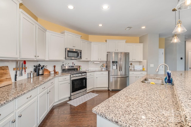 kitchen with appliances with stainless steel finishes, decorative light fixtures, dark hardwood / wood-style floors, sink, and white cabinets