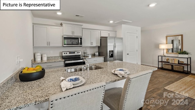 kitchen with light stone countertops, appliances with stainless steel finishes, sink, an island with sink, and dark hardwood / wood-style floors