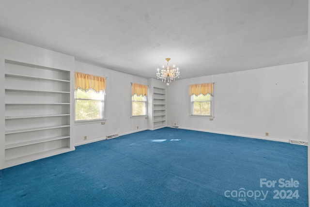 unfurnished room featuring a wealth of natural light, a chandelier, dark colored carpet, and built in shelves