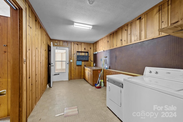 washroom with wood walls, a textured ceiling, a wealth of natural light, and washing machine and clothes dryer