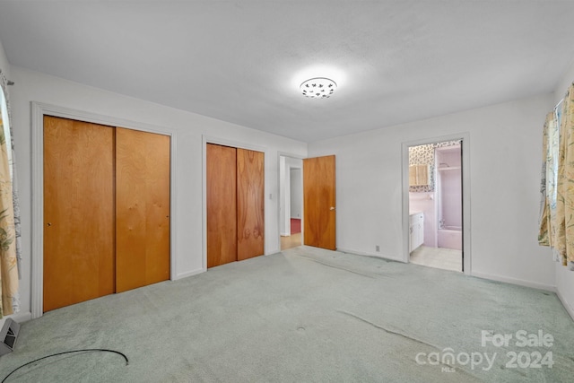 unfurnished bedroom featuring ensuite bath, two closets, and light colored carpet