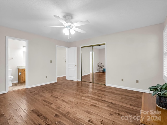 unfurnished bedroom with ceiling fan, a textured ceiling, hardwood / wood-style flooring, ensuite bathroom, and a closet