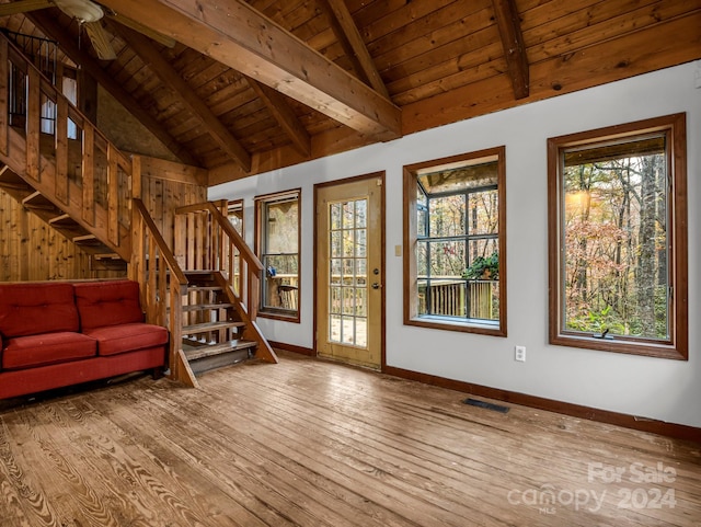 unfurnished living room with wood walls, wood-type flooring, lofted ceiling with beams, ceiling fan, and wooden ceiling