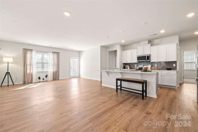 kitchen featuring a center island with sink, a breakfast bar area, appliances with stainless steel finishes, white cabinetry, and light hardwood / wood-style floors