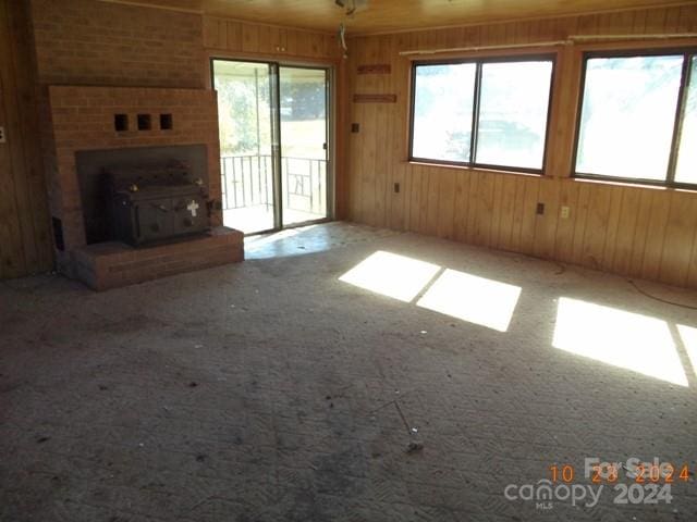 unfurnished living room featuring wooden walls, carpet, and a wood stove