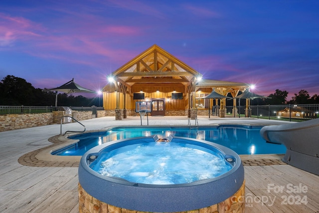 pool at dusk featuring a patio and an in ground hot tub