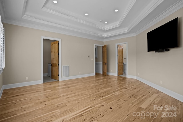 unfurnished bedroom featuring ensuite bathroom, a raised ceiling, light wood-type flooring, and ornamental molding