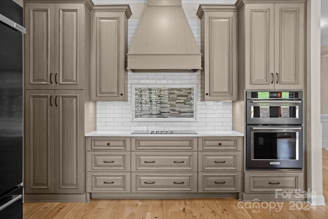 kitchen with decorative backsplash, appliances with stainless steel finishes, light hardwood / wood-style floors, and custom exhaust hood