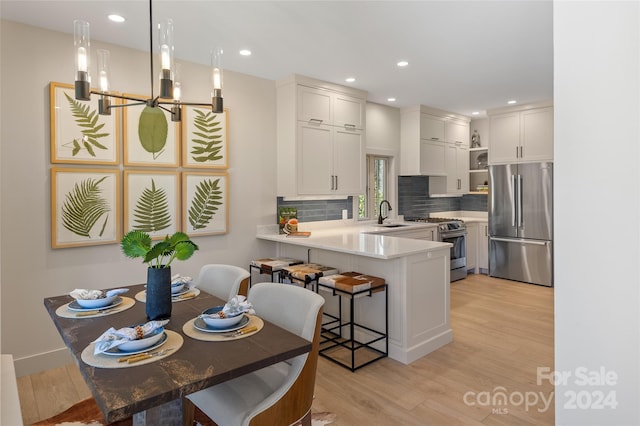 kitchen with appliances with stainless steel finishes, light wood-type flooring, kitchen peninsula, pendant lighting, and white cabinets