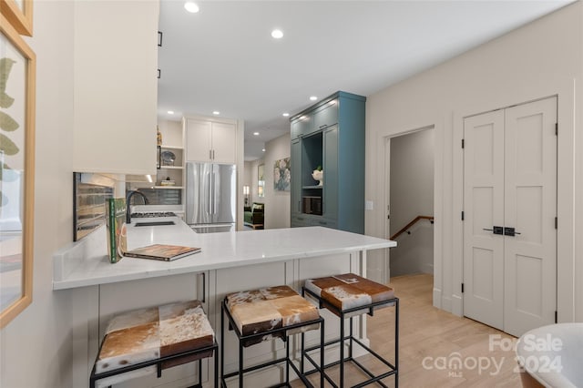 kitchen featuring kitchen peninsula, stainless steel fridge, a kitchen bar, light wood-type flooring, and white cabinets