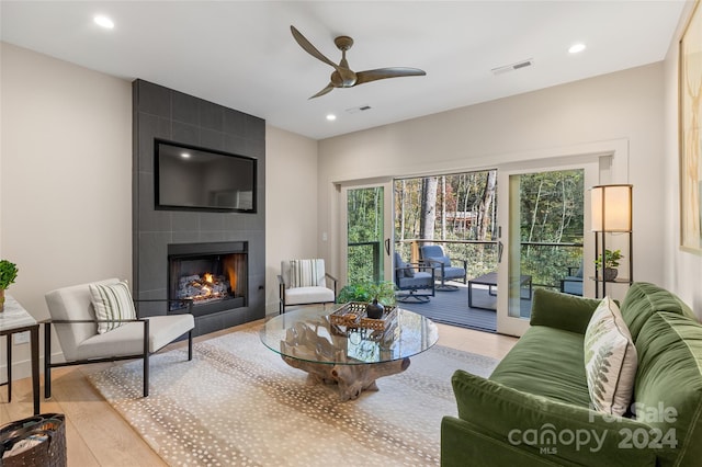 living room featuring light hardwood / wood-style floors, a tile fireplace, and ceiling fan