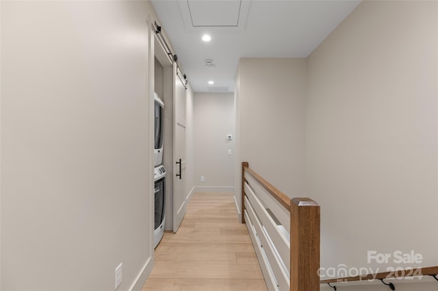 corridor with stacked washer and dryer, light hardwood / wood-style floors, and a barn door