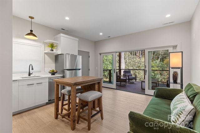 kitchen featuring sink, light wood-type flooring, hanging light fixtures, white cabinetry, and stainless steel appliances